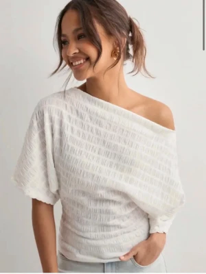Vit offshoulder topp från Nelly - Säljer en vit topp med offshoulder-design och korta ärmar. Materialet har en strukturerad yta 💕