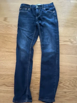 Mörkblå Levi's jeans med raka ben - Snygga mörkblå jeans från Levi's med klassisk femficksdesign och raka ben. Jeansen har kontrastsömmar och läderpatch bak i midjan. Perfekta för en avslappnad och stilren look.