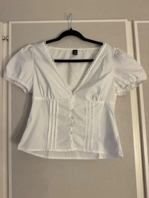 Vit topp med v-ringning och spetsdetaljer - Söt vit blus från Shein med korta puffärmar, v-ringning och spetsdetaljer längs halsringningen. 