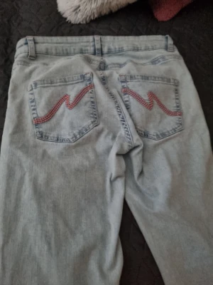 Ljusblå jeans med rosa detalj från nelly  - Säljer ett par ljusblå jeans med raka ben och coola rosa  zigzag-detaljer på bakfickorna. Klassisk femficksmodell med bälteshällor och knappgylf. Perfekta för en avslappnad och trendig look. Använd två gånger storlek 42 men passar 38-40 också köpte från nelly ljusblå 