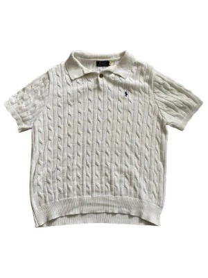 Vit Stickad Piké Ralph Lauren (prutbart) - Vit kabelstickad pikétröja från Polo Ralph Lauren med korta ärmar och klassisk krage. Tröjan har ribbstickade muddar och en liten broderad logga på bröstet. Perfekt för en preppy look och tillverkad i mjukt material.