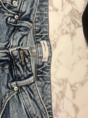 Blå bootcut jeans från gina - Säljer ett par klassiska blå bootcut jeans från Gina med snygga kontrastsömmar och broderade bakfickor. Jeansen har låg midja, bälteshällor och knappgylf. Perfekta för dig som gillar retrostil och vill ha ett par jeans med unik detalj på fickorna.