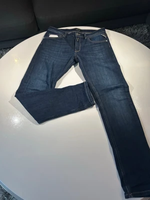 Mörkblå jeans från Replay - Snygga mörkblå jeans från Replay med klassisk femficksmodell och kontrastsömmar. Jeansen har smal passform och är tillverkade i ett slitstarkt denimtyg. Perfekta för dig som gillar en tidlös och stilren look.