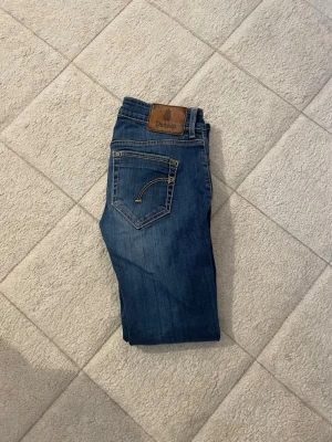 Blå jeans från Dondup - Snygga blå jeans från Dondup med klassisk femficksdesign och kontrastsömmar. Jeansen har en läderpatch med logga bak i midjan och cool detaljsöm på bakfickan. Perfekta för dig som gillar stilrena och tidlösa jeans.