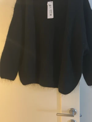 Svart fluffig kofta från Lindex - Mysig svart kofta från Lindex med öppen front och lång ärm. Koftan är fluffig och har en avslappnad passform, perfekt att slänga över en t-shirt eller topp. Enkel och stilren design som passar till det mesta.