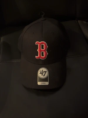 Svart Boston Red Sox keps - Snygg svart keps från '47 med klassisk Boston Red Sox-logga i rött och vitt framtill. Kepsen har böjd skärm och justerbar passform. Perfekt för dig som gillar sportig stil. Den är helt ny, jag har aldrig använt den, jag skulle skicka tillbaka den eftersom jag önskat mig två olika kepsar i julklapp då jag fick två och den andra var snyggare och mer i MIN stil. 