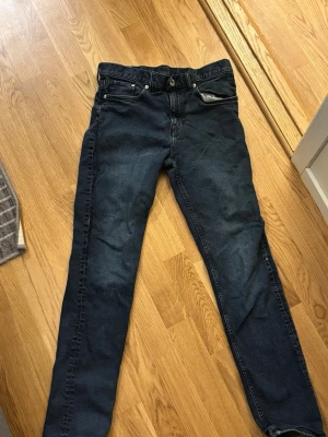 Mörkblå slim fit jeans - Säljer ett par mörkblå slim fit jeans med klassisk femficksdesign och dragkedjegylf. Jeansen har raka ben och är tillverkade i ett mjukt denimtyg som sitter snyggt. Perfekta för dig som gillar en enkel och stilren look.