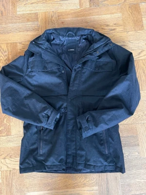 J.Lindberg field jacka  - Snygg svart jacka från J.Lindeberg med huva, dragkedja och tryckknappar. Jackan har två bröstfickor med lock och två sidofickor med dragkedja. Materialet är slitstarkt och jackan är fodrad för extra värme. Inga synliga defekter förutom att dragkedjan inte fungerar men det är ändå snyggare när man använder knapparna som finns!