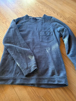 Grå sweatshirt från Human Scales - Mysig grå sweatshirt från Human Scales i japanskt tyg. Tröjan har en bröstficka med knapp och klassisk rund hals. Perfekt för en avslappnad stil .