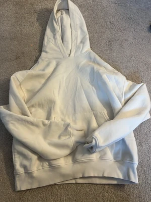 Vit hoodie från Gina  - Snygg vit hoodie med klassisk huva och magficka. Perfekt för en avslappnad stil och enkel att matcha med jeans eller joggers. Mjuk bomullskänsla och ribbade muddar vid ärmslut och nederkant. 
