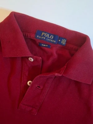 Röd piké från Polo Ralph Lauren - Säljer en röd pikétröja från Polo Ralph Lauren i slim fit. Klassisk krage, korta ärmar och två knappar framtill. Tillverkad i mjuk bomull och har den ikoniska broderade loggan på bröstet. Perfekt för en clean och stilren look. Tveka inte o höra av er vid frågor/funderingar