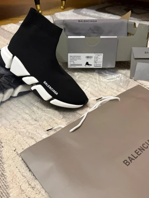 Balenciaga Speed Trainer  - Svarta Balenciaga Speed Trainer sneakers med vit chunky sula och stickad strumpliknande ovandel. Minimalistisk design med Balenciaga-logga på sidan. Skorna har en elastisk passform och är tillverkade i textil och gummi för en futuristisk look.
