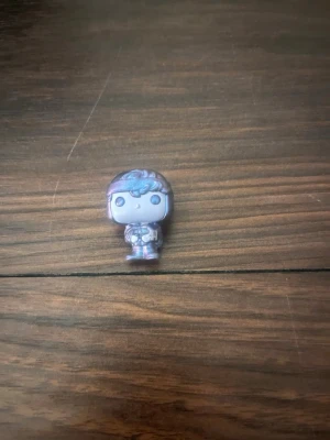 Liten Funko Pop-figur  - Säljer en liten Funko Pop-figur i metallic lila och blå nyanser. Figuren har stora ögon, detaljerat hår och bär en dräkt med bälte. Perfekt för samlare eller som dekoration på skrivbordet.