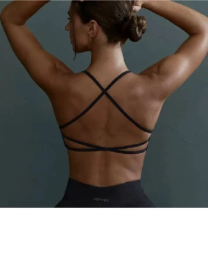 Svart sport-bh med korsade band - Snygg svart sport-bh från Bo+tee med tunna axelband och korsade band i ryggen. Bh:n har en stilren design med diskret logga framtill och är tillverkad i ett stretchigt material som passar perfekt för träning.