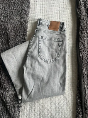 Grå raka jeans från bik bok.  - Snygga grå jeans från bik bok med raka ben och klassisk femficksmodell. Jeansen har en ljusgrå tvätt och ett brunt läderpatch med logga bak i midjan. Tillverkade i mjukt denimtyg som ger en avslappnad look.