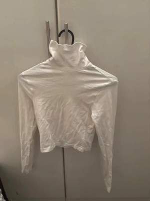 Vit croppad polotopp - Säljer en vit croppad polotopp med lång ärm. Toppen har en hög polokrage och är tillverkad i mjuk bomull, perfekt för att styla lager på lager. Enkel och clean design som passar till det mesta. För mer bilder/justering av pris skriv gärna❤️🤗 (strykning inkluderar jag gratis)