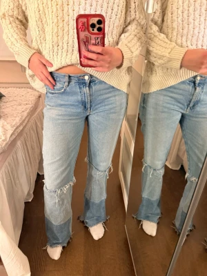 Ljusblå patchwork jeans med slitningar - Säljer ett par ljusblå jeans med patchwork-detaljer och råa, slitna kanter vid knän och benslut. Jeansen har rakaben och klassisk femficksmodell. Perfekta för en avslappnad och trendig look.