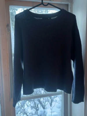 Svart stickad tröja med rund hals - En enkel och stilren svart stickad tröja med rund halsringning och långa ärmar. Tröjan har en rak passform och är perfekt för lager på lager. Passar till det mesta och är ett måste i garderoben. Den är ganska nopprig (därav priset) 