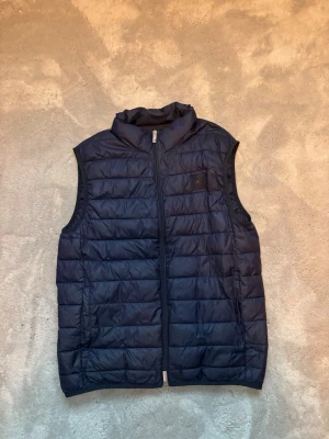 Mörkblå dunväst med dragkedja från Purificación García - Snygg mörkblå dunväst. Västen har dragkedja framtill och två sidofickor. Perfekt för lager-på-lager och ger en sportig look. Passar till både jeans och hoodie för en chill stil.