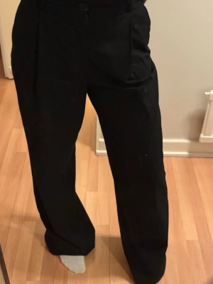 Svarta vida kostymbyxor - Säljer ett par svarta kostymbyxor med hög midja och vida ben. Byxorna har pressveck framtill, sidfickor och knappstängning i midjan. Perfekta för en clean och stilren look. Från Zara i storlek xs