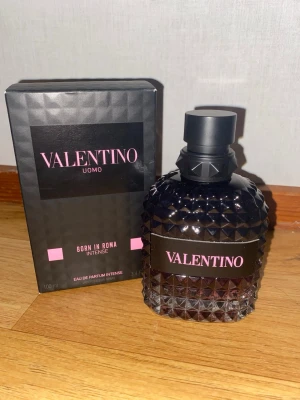 Valentino Uomo Born In Roma Intense 100ml - Valentino Uomo Born In Roma Intense är en lyxig parfym i en svart och rosa designad flaska med nitar och diamantmönster. Doften kommer i en elegant svart kartong med rosa detaljer och rymmer 100 ml Eau de Parfum Intense. Perfekt för dig som gillar exklusiva och moderna dofter.