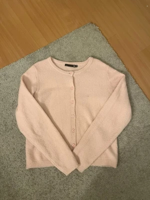 Ljusrosa kofta från 157 med knappar - Söt ljusrosa kofta från 157 i storlek XS. Koftan har rund halsringning, långa ärmar och stängs med matchande rosa knappar framtill. Perfekt att slänga över en topp för en enkel och stilren look. (Liten fläck bild 2)