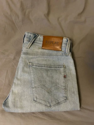Ljusblå jeans från Replay - Säljer ett par ljusblå jeans från Replay med klassisk femficksdesign och snyggt läderpatch bak i midjan. Storlek W30 Slim fit. Små skav nere vid benslutet (se bild 4). Hör av dig vid prisförslag eller frågor😁