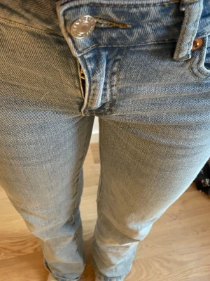 Ljusblå raka jeans med knappgylf - Säljer ett par ljusblå jeans med rak passform och midium midja. Klassisk femficksmodell med knappgylf och subtila slitningar. Perfekta till sneakers eller boots för en avslappnad look.
