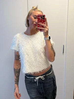 Vit fluffig topp från Kappahl - Superfin vit topp från Kappahl med fluffig textur och kort ärm. Croppad modell som ger en trendig look, perfekt att styla med höga jeans eller kjol. Mjuk och skön, passar dig som gillar unika detaljer.