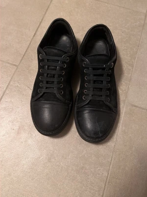 Lanvins Svarta låga sneakers i mocka - Säljer ett par helsvarta lanvin sneakers med lågt skaft. Skorna har ovandel i mocka och tåparti i läder, samt svarta skosnören och metallöljetter. Klassisk och stilren design som passar till det mesta. Skick är bra. Lite små defekter (se på bilderna) hör av dig vid frågor. Inget og ingår tyvärr😊OBS priset är inte hugget i sten!!