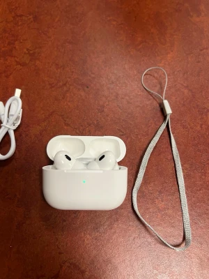Apple AirPods Pro med laddningsetui - Säljer ett par vita Apple AirPods Pro med trådlöst laddningsetui. Hörlurarna har en stilren och kompakt design i blank plast. Medföljer gör en vit USB-C laddningskabel och en silverfärgad handledsrem. Perfekta för musik, poddar och samtal. Aldrig använda eftersom min pappa köpte fel modell och gick inte att lämna tillbaka 