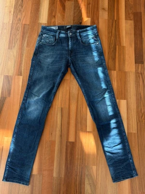 Mörkblå slim fit jeans från Replay Anbass - Säljer ett par mörkblå slim fit jeans från Replay med snygga slitningar och tvättade detaljer. De är modellen anbass, säljer pga dom är för små! 