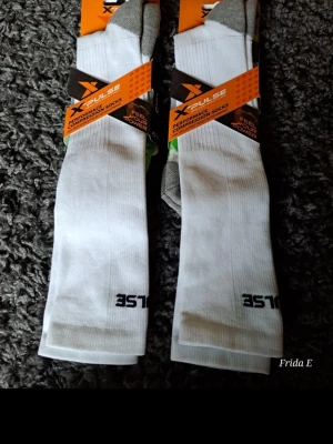 Vita kompressionsstrumpor X-Pulse 2 par - Säljer ett par vita kompressionsstrumpor från X-Pulse med grå tå och häl samt svarta detaljer. Strumporna är tillverkade i en blandning av bomull, polyester och elastan, perfekta för träning och sportiga aktiviteter.