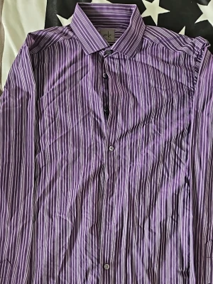 Lila randig skjorta från Calvin Klein - Snygg lila skjorta från Calvin Klein i slim fit-modell. Skjortan har ett randigt mönster i olika nyanser av lila och vitt, klassisk krage och knäppning framtill. Tillverkad i mjuk bomull som känns skön mot huden. Perfekt för dig som gillar stilrena detaljer.