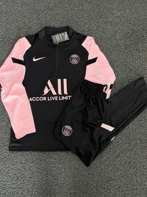 PSG träningsset FÖRBESTÄLLING ENDAST  - Snyggt PSG träningsset från Nike i svart med rosa detaljer. Tröjan har halv dragkedja, lång ärm och klubbmärke på bröstet. Byxorna är svarta med PSG-logga och rosa detalj. Perfekt för fotbollsträning eller chill. Helt nytt, fraktar inom 24 timmar 