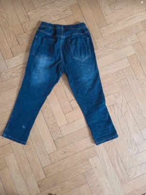 Blå 3 / 4 dels långa stretchjeans med resårmidja stl 38  - Snygga blå jeans 3 / 4 dels benlängd  med resår i midjan och raka ben. Jeansen har två bakfickor och är gjorda i ett stretchigt denimtyg som ger en avslappnad och bekväm passform. Perfekta för en chill och enkel stil.INNERBENSMÅTT CA 57 CM , MÅTT FRÅN MIDJA OCH NER CA 84 CM , MIDJEMÅTT RAKT ÖVER CA 32 CM , EN LITEN VIT FLÄCK I TYGET LÄNGST NER PÅ BYXBENET ( SE BILDEN )