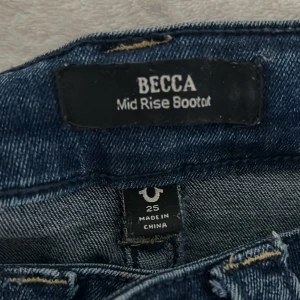 True Religion Becca Bootcut Jeans - Snygga blå bootcut jeans från True Religion, modell Becca Mid Rise. Jeansen har klassisk femficksdesign, coola broderade bakfickor med vita detaljer och guldiga knappar. Tillverkade i stretchig denim för skön passform och med en låg  midja. Jag har sytt de low waist som även gör att benen blir lite mindre (låren).