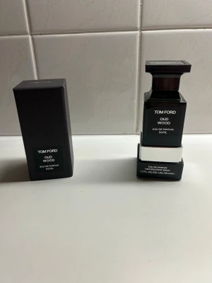 Tom Ford Oud Wood Eau de Parfum 50ml - Tom Ford Oud Wood Eau de Parfum i en elegant, mörkgrå fyrkantig glasflaska med svart lock. Flaskan rymmer 50 ml och har en lyxig och stilren design. Kommer med originalförpackning. En exklusiv doft med träiga och orientaliska toner.