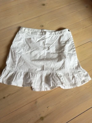 Vit volangkjol från POP - Säljer en söt vit kjol från POP med volangkant nedtill. Kjolen har en enkel design där man kan öppna upp hela och anpassa midjans storlek till ens passform. Perfekt till sommaren!! Går även då att bära som tube topp om man så vill😜