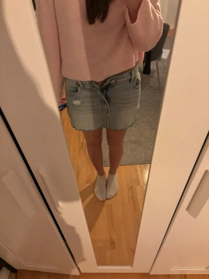 Ljusblå jeanskjol med slitningar - Trendig ljusblå jeanskjol med rå kant och slitna detaljer framtill. Kjolen har klassisk femficksdesign och knappgylf. Perfekt för dig som vill ha en avslappnad och cool stil.