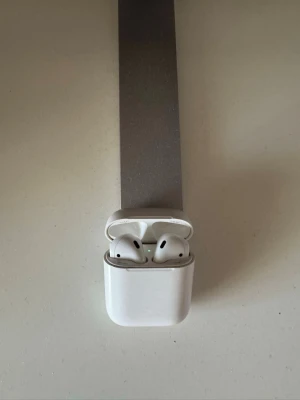 Apple AirPods med laddningsetui - Trådlösa vita Apple AirPods med klassisk minimalistisk design och laddningsetui i blank plast. Perfekta för musik, samtal och poddar med smidig Bluetooth-anslutning. Laddningsetuiet är kompakt och lätt att ta med sig. Använts under en lång period och behöver ej de längre så säljer