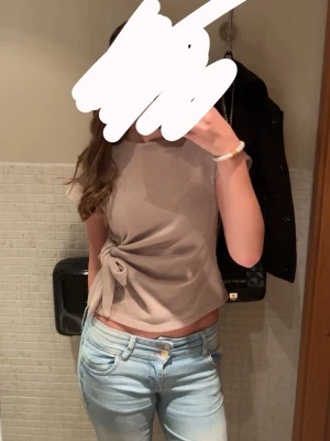 Beige topp med knyt från Zara - Trendig beige topp från Zara med korta ärmar och rund hals. Toppen har en snygg knytning i sidan som ger en cool twist till outfiten. Perfekt att matcha med jeans eller kjol för en avslappnad men stilsäker look.