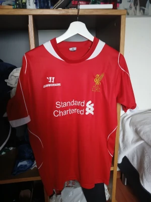 Liverpool matchtröja Warrior röd - Säljer en röd Liverpool FC matchtröja från Warrior med klubbmärke och sponsortryck på bröstet. Tröjan har vita detaljer vid krage och ärmslut samt tunna vita linjer längs sidorna. Perfekt för dig som älskar fotboll och vill visa ditt stöd för LFC. Slitage på numer 45 och lite på ballotelli. Men annars i bra skick.