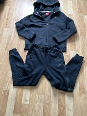 Svart hoodie från Nike med dragkedja - Säljer en svart hoodie från Nike med dragkedja framtill och huva. Hoodien har diskret Nike-logga på bröstet och är gjord i mjukt, bekvämt material. Perfekt för en avslappnad och sportig stil. Passar till både träning och chill.