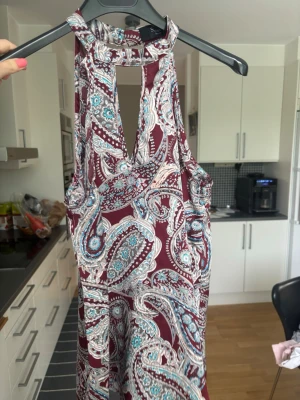 Mönstrad ärmlös topp med halterneck - Säljer en snygg ärmlös topp från Sisters Point med halterneck och djup v-ringning. Toppen har ett paisleyinspirerat mönster i vinrött, vitt och turkost. Perfekt för sommardagar och enkel att styla med jeans eller kjol.