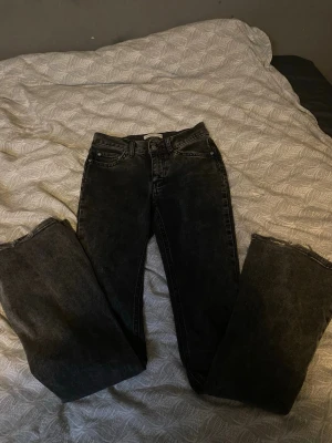 Svarta utsvängda jeans med rå kant - Säljer ett par svarta bootcut jeans med snygg tvätt och råa kanter nertill. Jeansen har klassisk femficksmodell och mid waist. Perfekta för en avslappnad och trendig look. Materialet är kraftig denim i bomull.