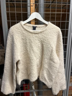 Krämvit fluffig stickad tröja Lindex - Mysig krämvit stickad tröja från Lindex med fluffig, texturerad yta och rund halsringning. Tröjan har en avslappnad passform och långa ärmar, perfekt för kalla dagar. 