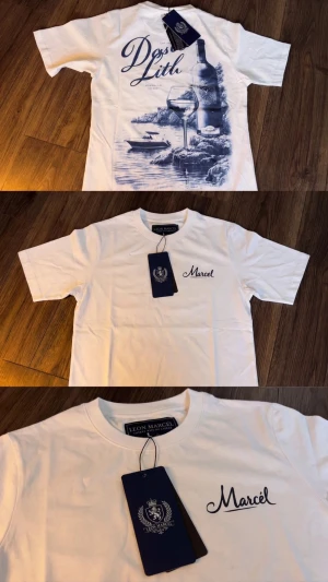 Vit t-shirt från Leon Marcel - Snygg vit t-shirt från Leon Marcel med tryck på ryggen som visar vinflaska, glas och havsmotiv i blått. Framtill står det 'Marcel' broderat i blått. Klassisk passform och rund hals. Perfekt för dig som gillar stilrena plagg med unik detalj på ryggen.