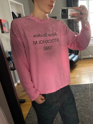 Rosa longsleeve Acne Studios - Säljer en rosa långärmad topp från Acne Studios med tryck på bröstet där det står 'Acne Studios STOCKHOLM 1996' spegelvänt. Toppen har en loose passform och är gjord i mjuk bomull. Perfekt för dig som gillar streetwear och vill ha något unikt i garderoben.