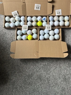 Stort paket med "Övningsbollar från EliteTee - Säljer ett stort paket med golfbollar från EliteTee, blandade märken som Callaway. Bollarna är mestadels vita men några är gula. Levereras i kartonger, perfekta för golfträning eller spel. Materialet är klassisk hård plast och designen är traditionell med dimple-mönster.
